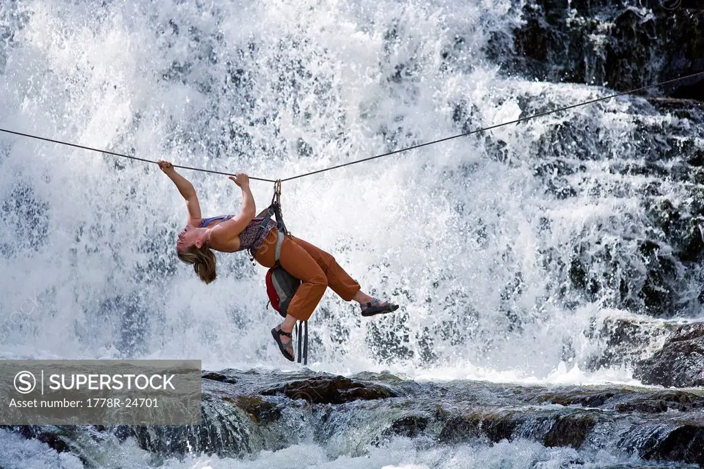 A woman crosses a waterfall using a Tyrolean Traverse on a rope.