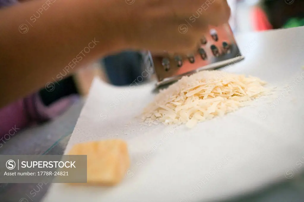 Selective focus view of a person shredding hard cheese on a grater.