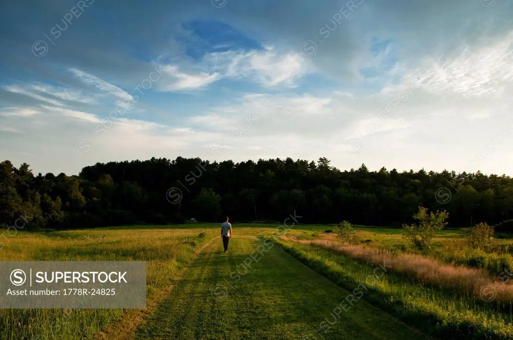 A young man strolls down a grassy road during the evening light outside Acadia National Park, Maine.