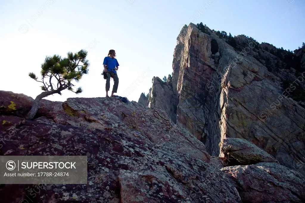 A young adult stands triumphantly on top of a 500 ft multi pitch trad climbing route in Colorado.