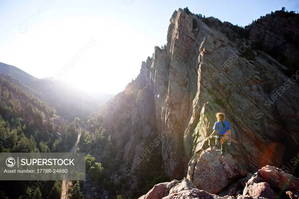 A young adult stands triumphantly on top of a 500 ft multi pitch trad climbing route in Colorado.