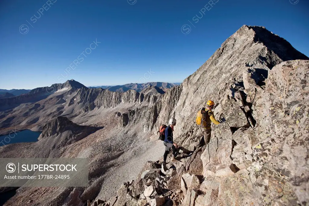 Two young men crossing an exposed ridge line with the summit behind them.