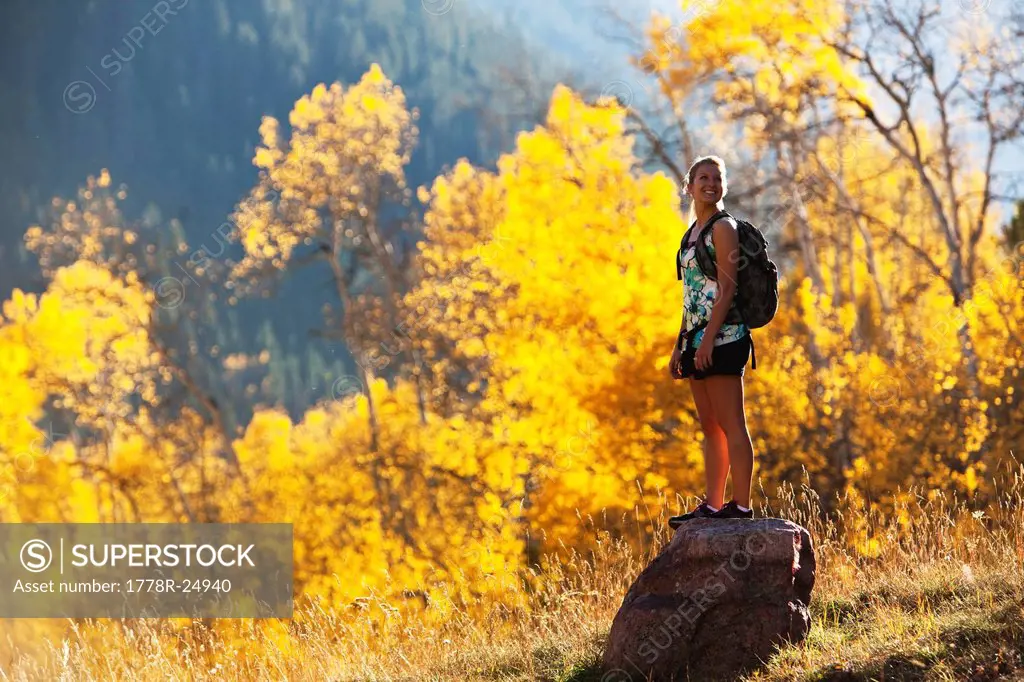 A young woman hiking stops and enjoys the beauty of the golden fall colors.