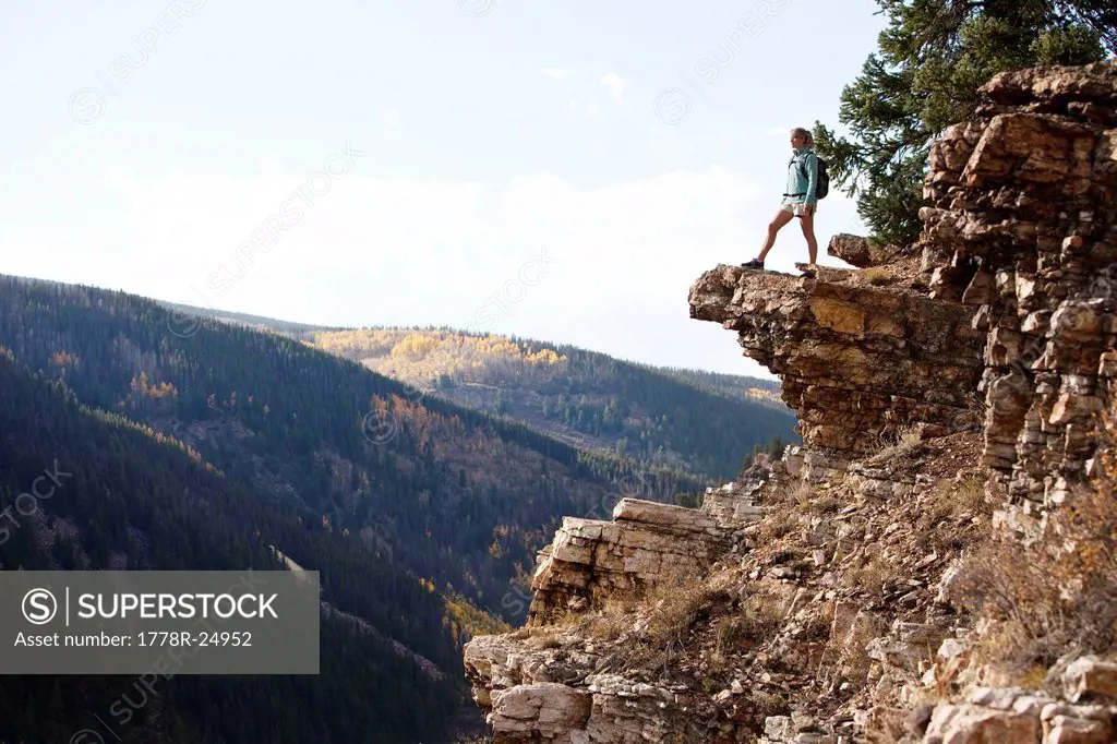A young woman hiking takes a look over the edge of the canyon.