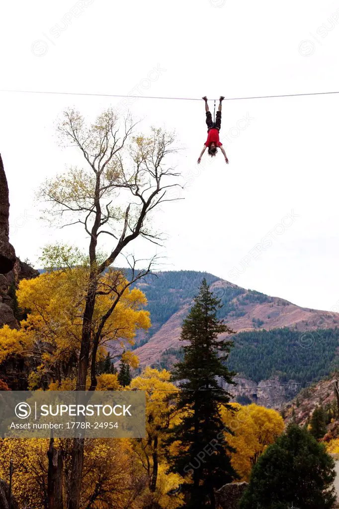 A young man does a bat hang from a slack line after walking the line.