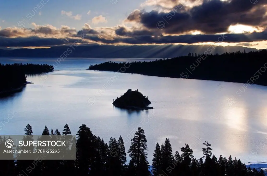 Rays of sunlight penetrate the clouds behind Emerald Bay at sunrise in Lake Tahoe, CA.