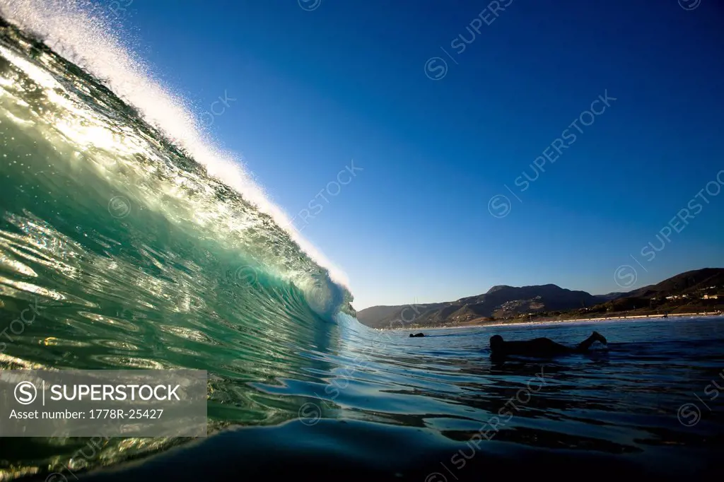 A male surfer gets ready to duck dive a backlit wave while surfing Zuma Beach in Malibu, California.