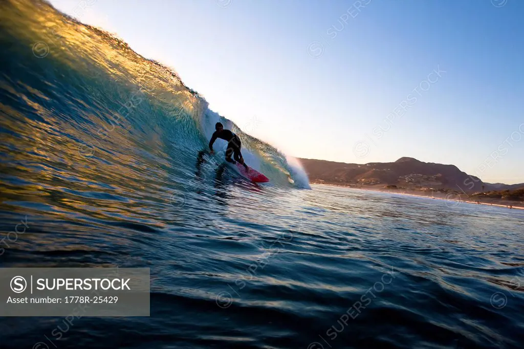 A surfer riding a red surfboard sets up for a barrel while surfing at Zuma Beach in Malibu, California.