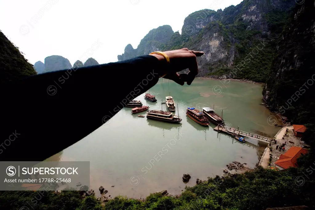 A climber points to limestone cliffs in Halong Bay, Vietnam. Halong Bay has thousands of climbable limestone formations throughout the bay making this...