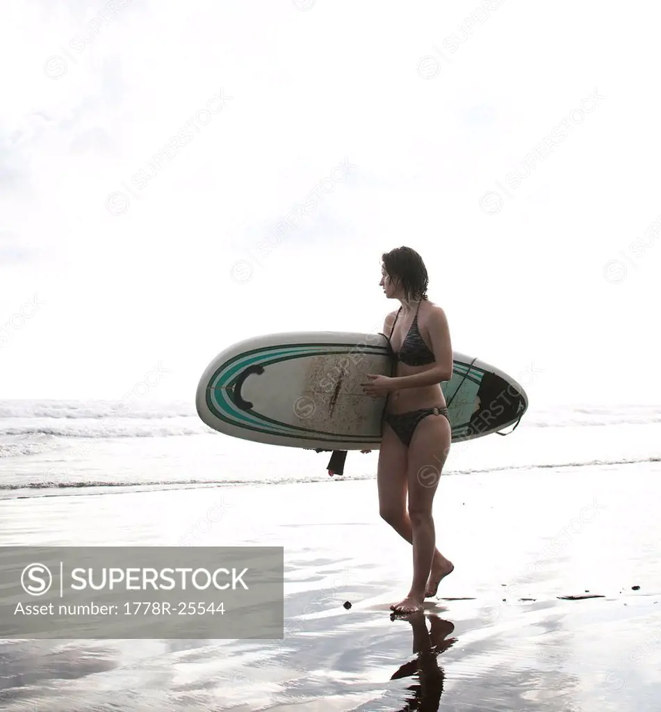 A woman walks on the beach carrying her surfboard.