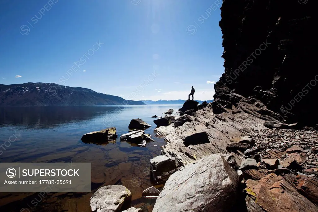 A male figure stands on a rock at the edge of a beautiful lake on a sunny day in Idaho.