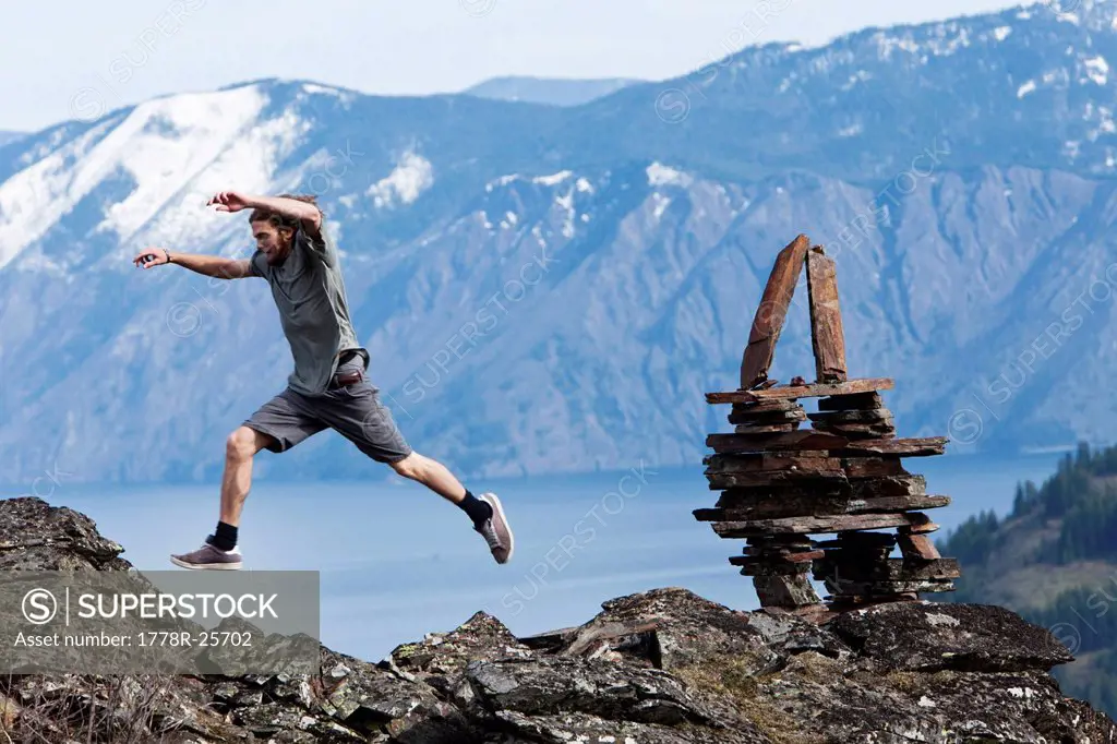 A young man leaps next to a balanced rock stack high above a mountain lake in Idaho.