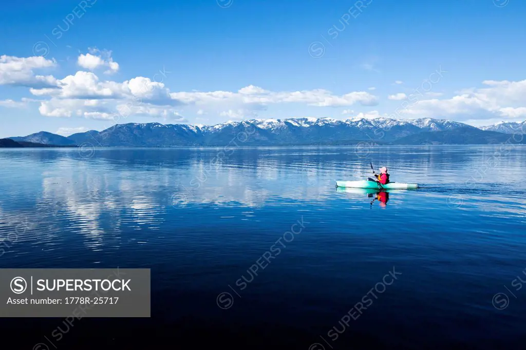 An adventurous women kayaking across a huge calm lake in Idaho.