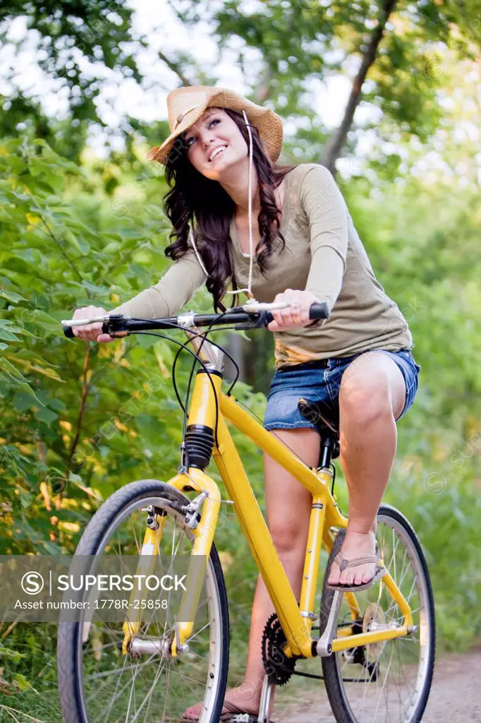 A smiling young woman rides a yellow bike down a dirt road.