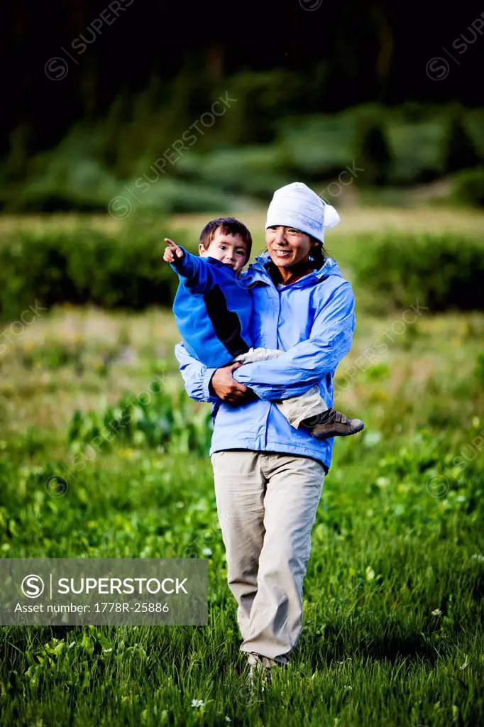 A woman walks through a meadow at Squaw Pass holding her 2 year old son.