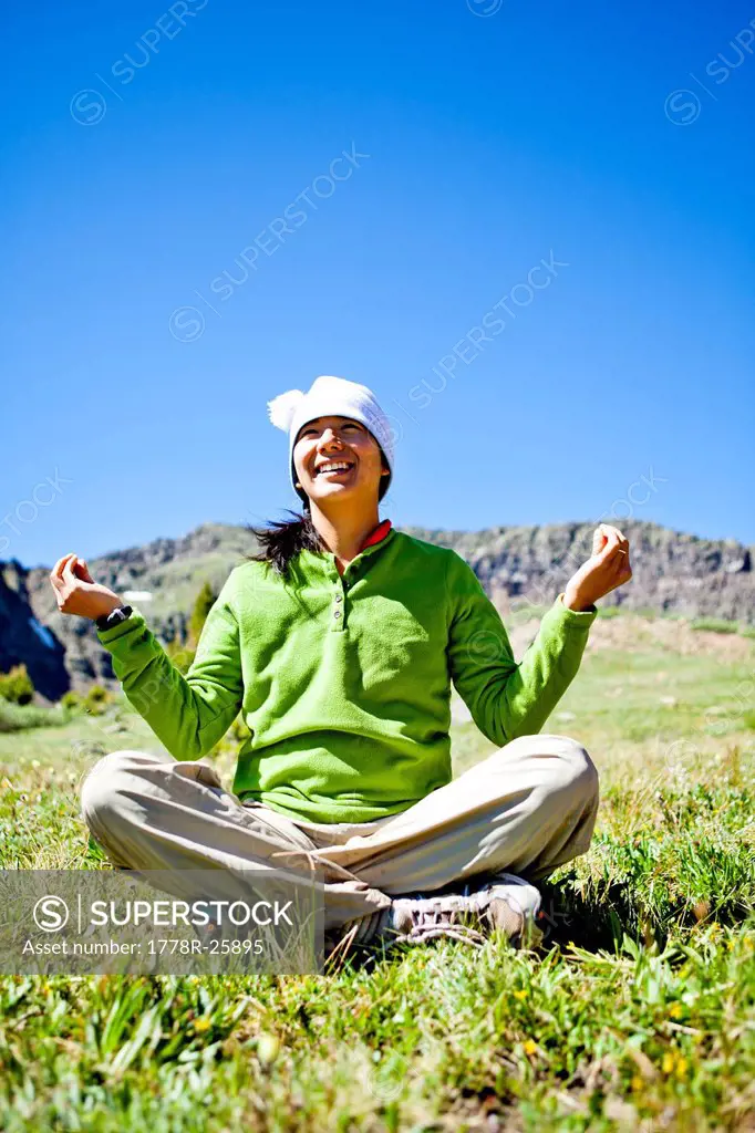a woman smiles as she sits cross legged in an alpine meadow with wildflowers doing a Buddha pose. They are just off the Continental Divide Trail CCT, ...