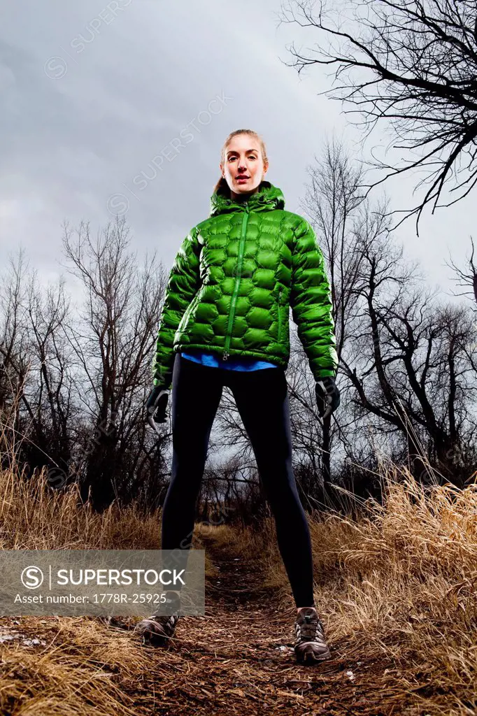 Environmental Portrait of a young woman standing on a running trail in a green jacket in the winter time.