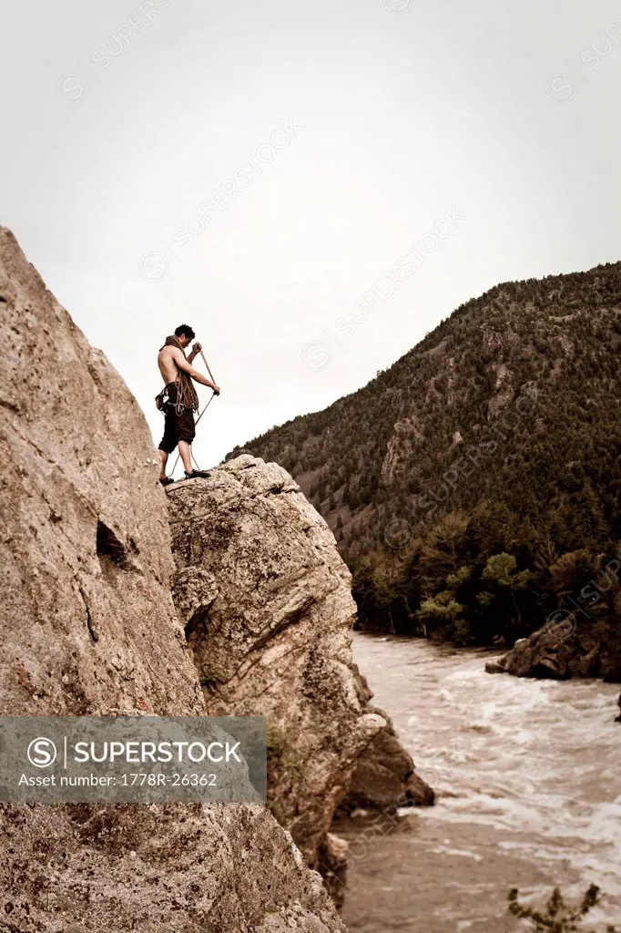 A athletic man coils a rock climbing rope next to a river in Montana.