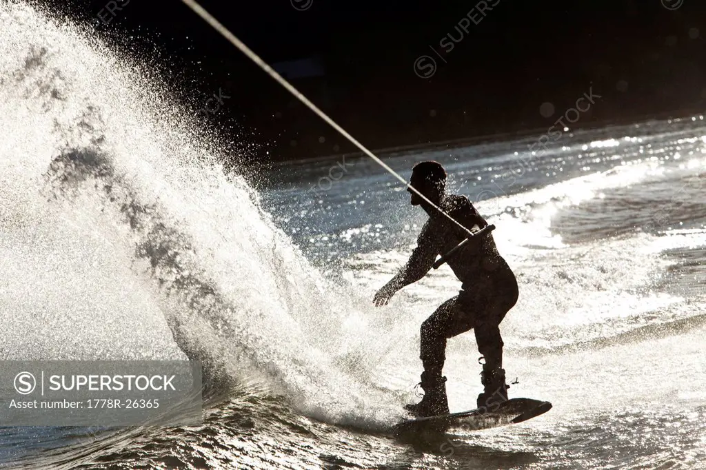 A professional wakeboarder carves and slashes on a lake at sunset in Idaho.