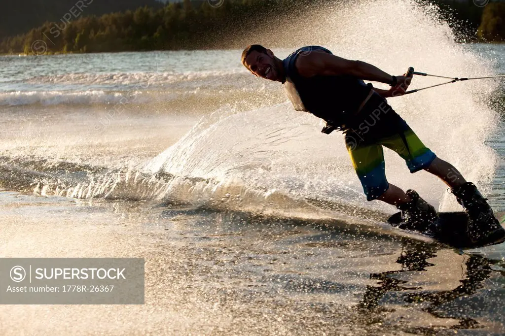 A professional wakeboarder smiles while he carves and slashes on Lake Pend Oreille at sunset in Sandpoint, Idaho.