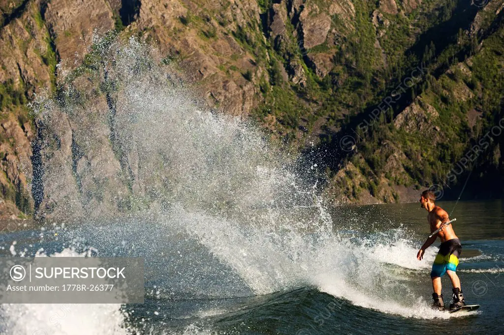 A athletic male wakeboarder carves and slahes the wake at sunset on a lake in Idaho.