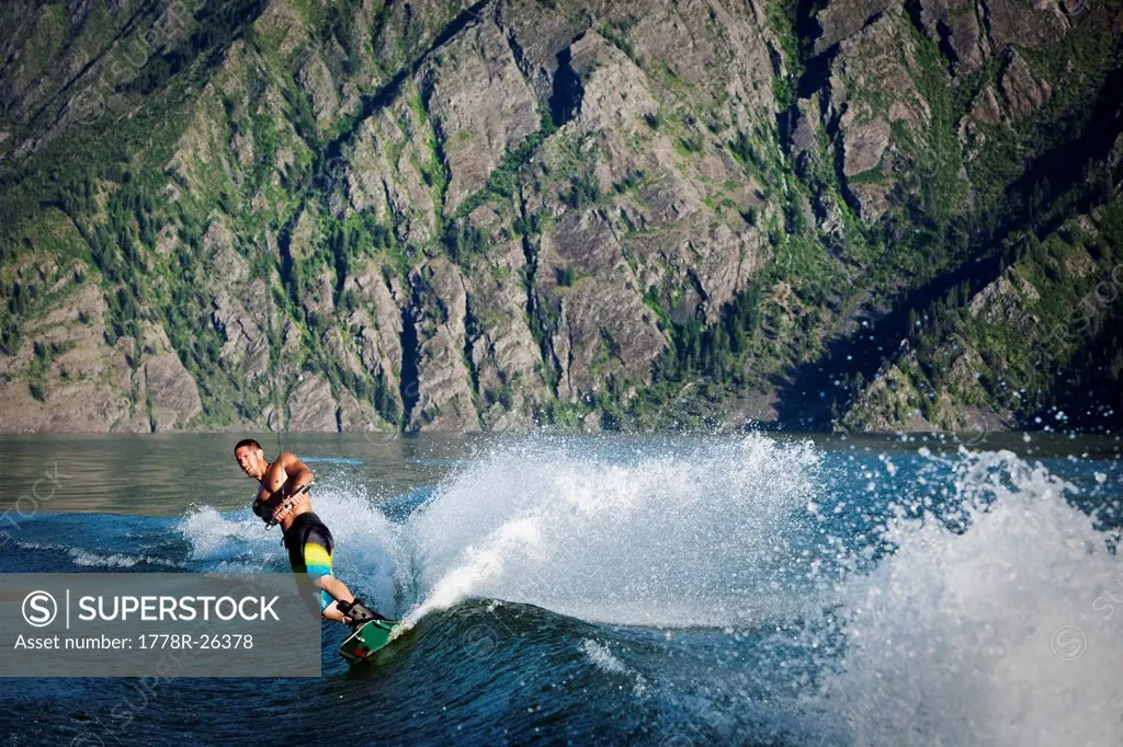 A athletic male wakeboarder carves and slahes the wake at sunset on a lake in Idaho.