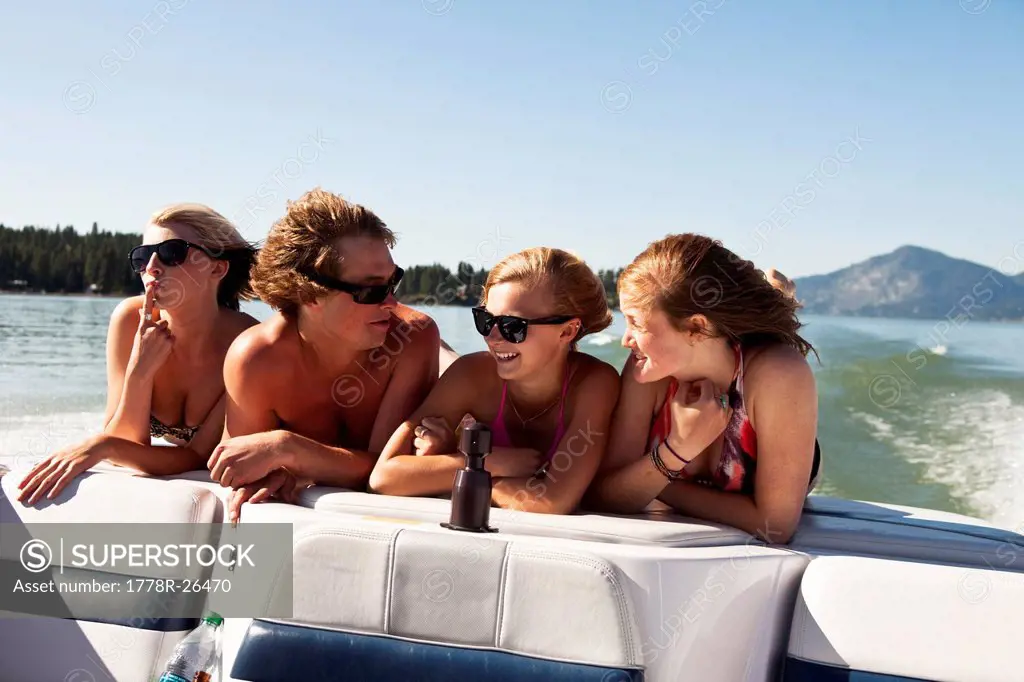 Four young adults laughing and smiling on the back of a wakeboard boat on a lake in Idaho.