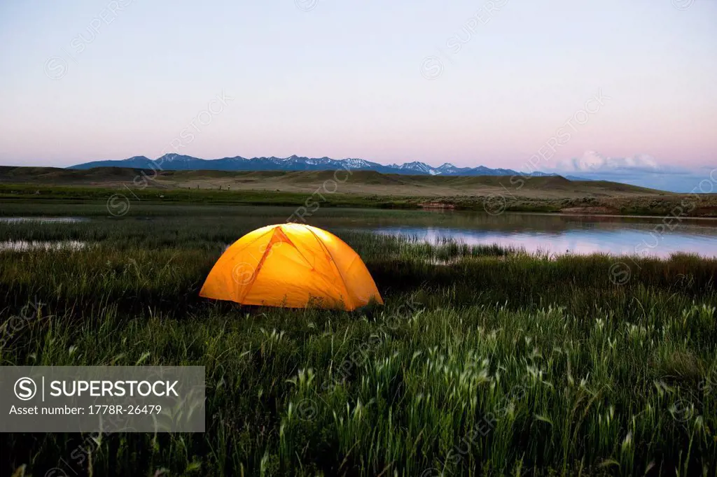 A glowing tent next to a lake at sunset in Montana.
