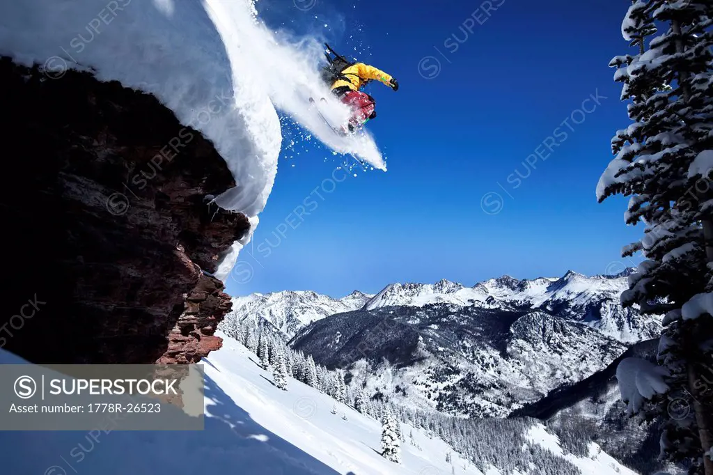 A athletic skier jumping off a cliff in the backcountry on a sunny powder day in Colorado.