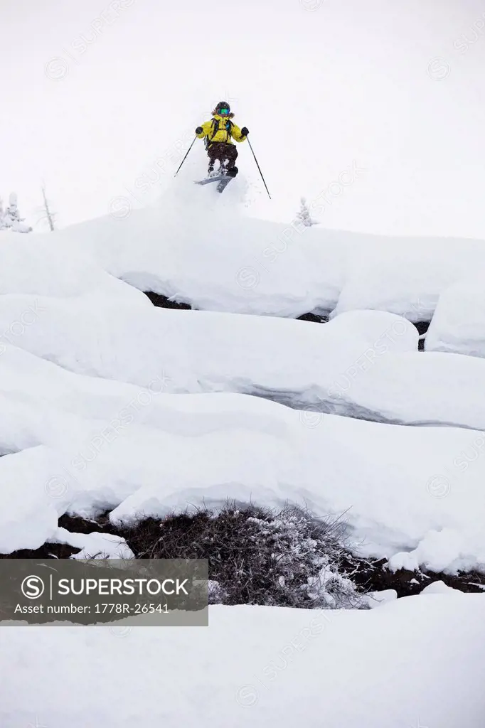 A female skier jumping off a cliff on a stormy day in Colorado.