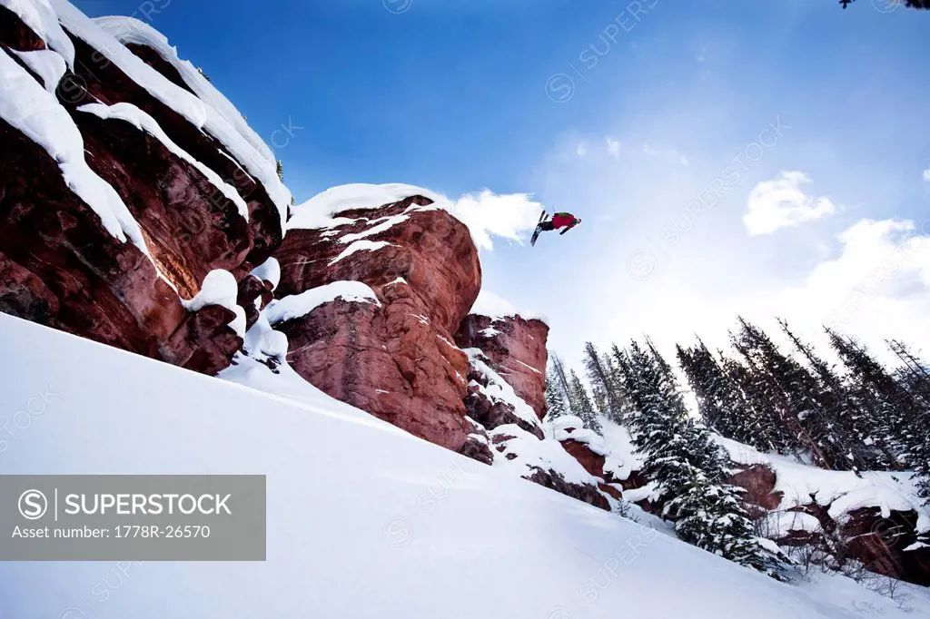 A athletic skier flipping off a cliff in the backcountry on a sunny powder day in Colorado.