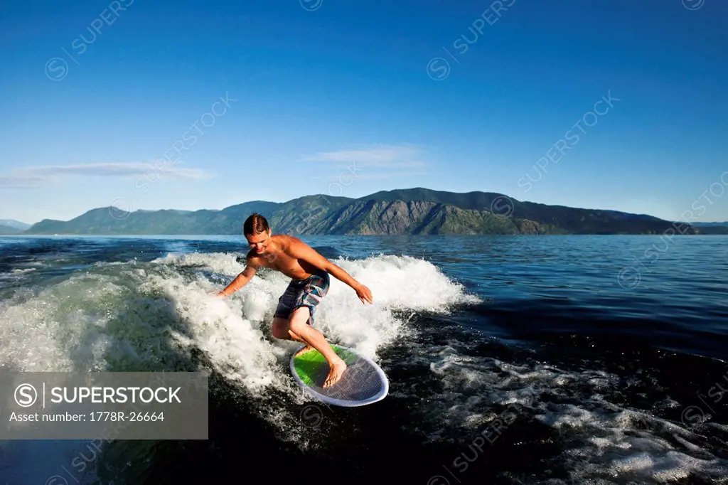 A happy man smiles while wakesurfing behind a wakeboard boat on a sunny day in Idaho.
