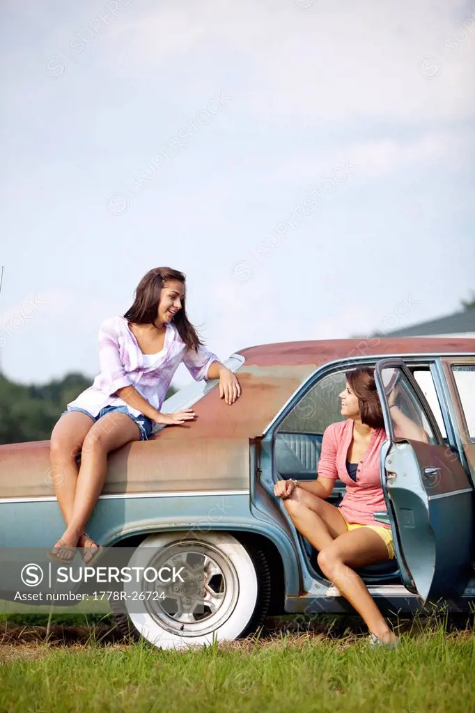 Two sisters hang out on a classic car.