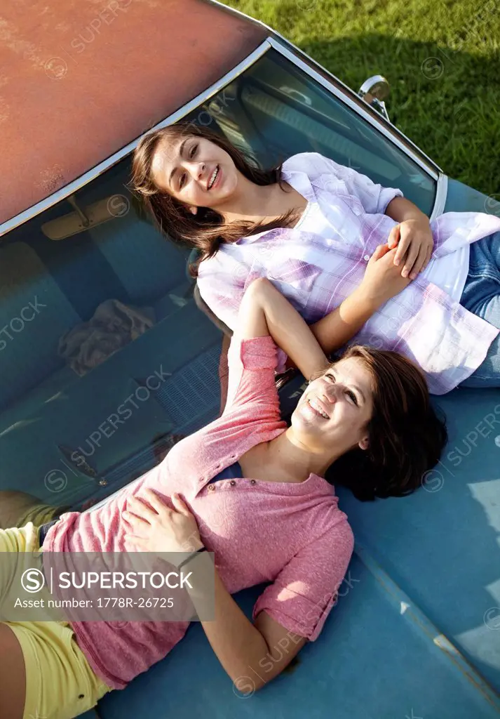 Two sisters lay on the hood of an old car.