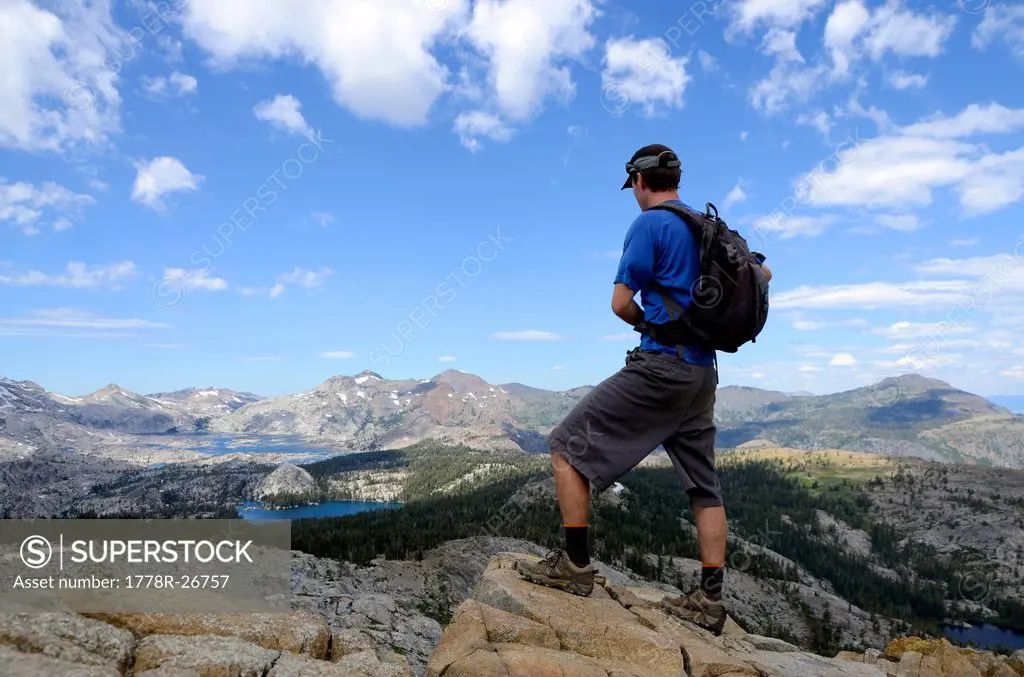 A male hiker stands on the summit of Mount Ralston looking over Desolation Wilderness in the summer, CA.