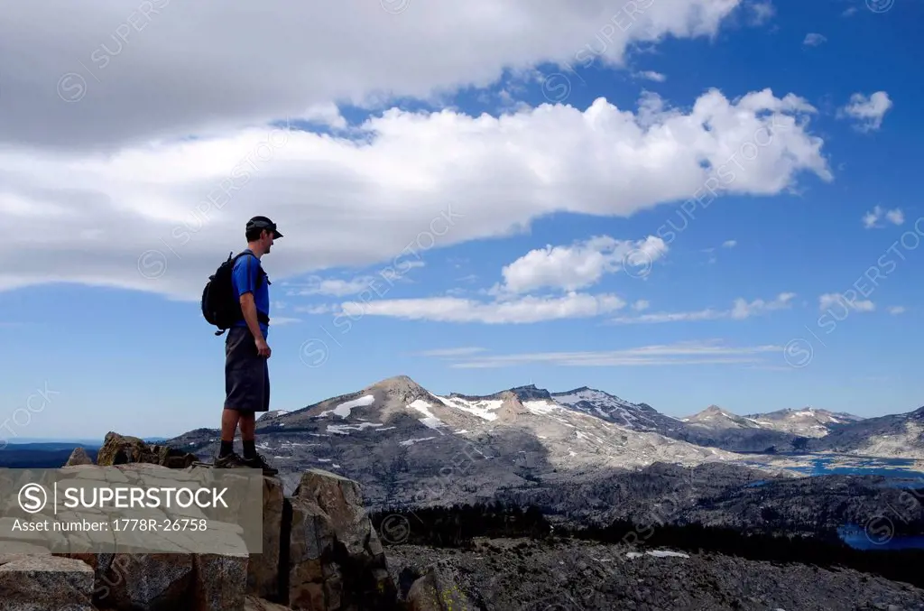 A male hiker stands on the summit of Mount Ralston looking over Pyramid Peak and Desolation Wilderness in the summer, CA.