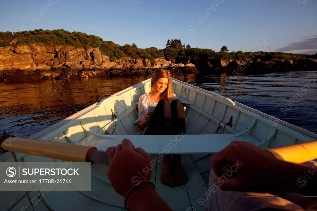 A teen girl in a dinghy reads a journal as the glow of the setting sun warms her face.