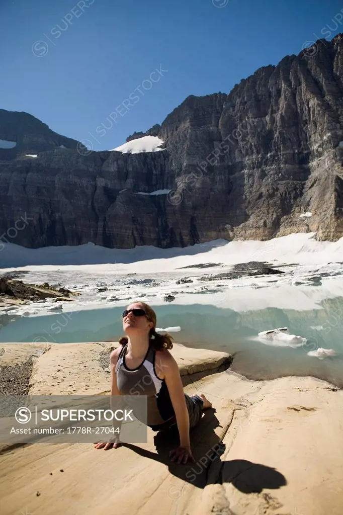 A woman in her early thirties strikes an upward dog yoga pose at the Grinnell Glacier in Glacier National Park, Montana.