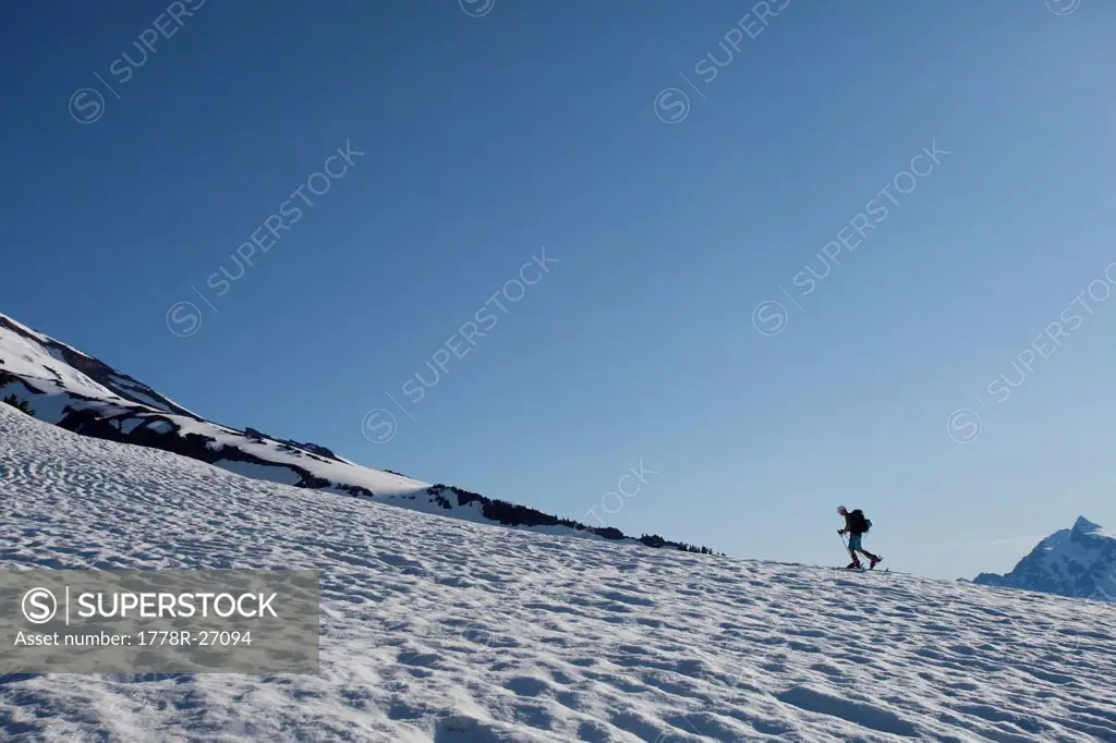 A lone skier skins up a snowy ridge at sunrise on a blue bird day.
