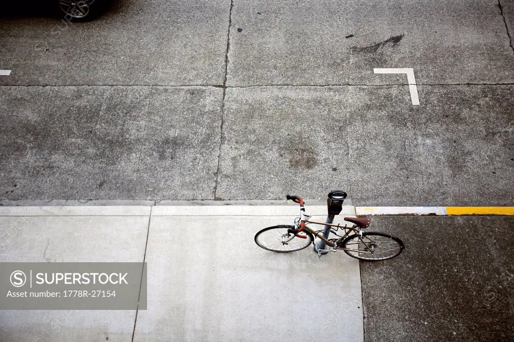 A bicycle is secured to an empty car parking space and a city parking meter.