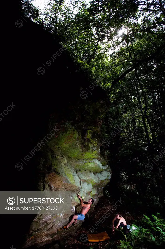 A male climber ascends an overhanging rock feature deep in the forests of Ibbenburen, Germany.