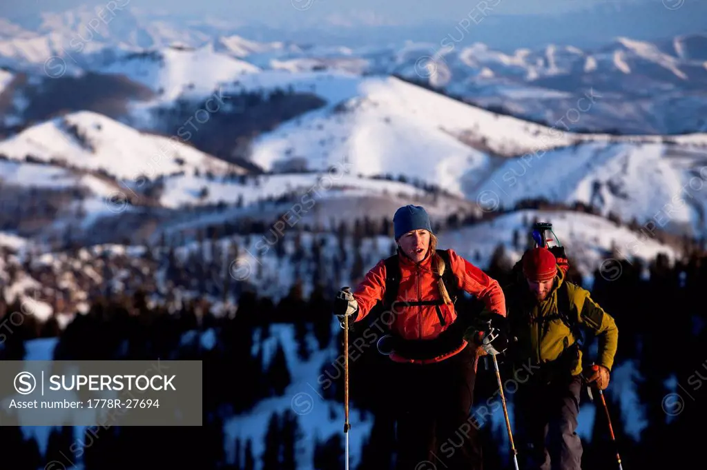 Man and woman backcountry skiers reaching their summit in beautiful sunrise light.