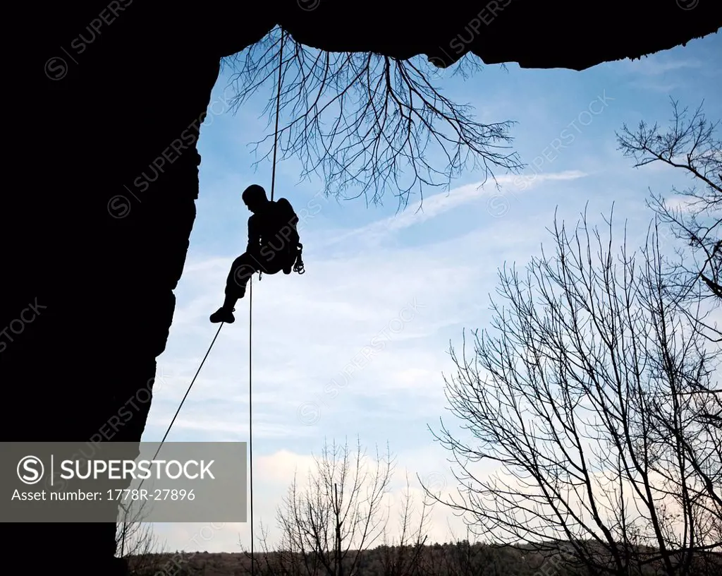 A climber rappels down from the side of a cliff silhouette.