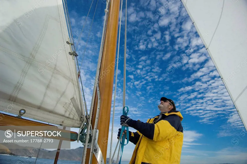 A man adjusts the rigging on his yacht.