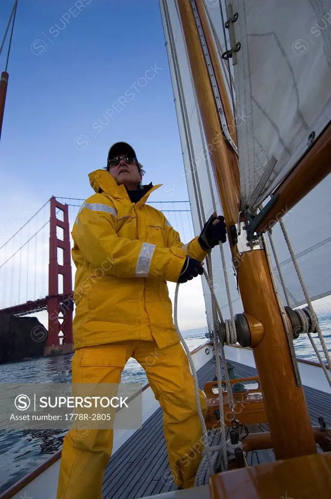 A man adjusts the rigging on a yacht.