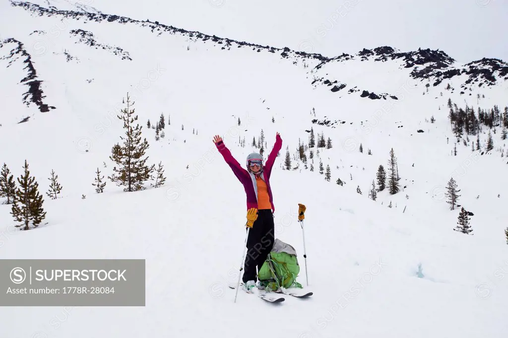 A skier raises her arms in celebration while climbing a mountain on a snowy day in the Cascades.
