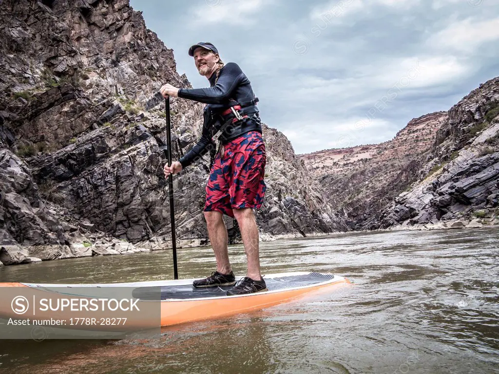 A man stand up paddle boarding on a river.