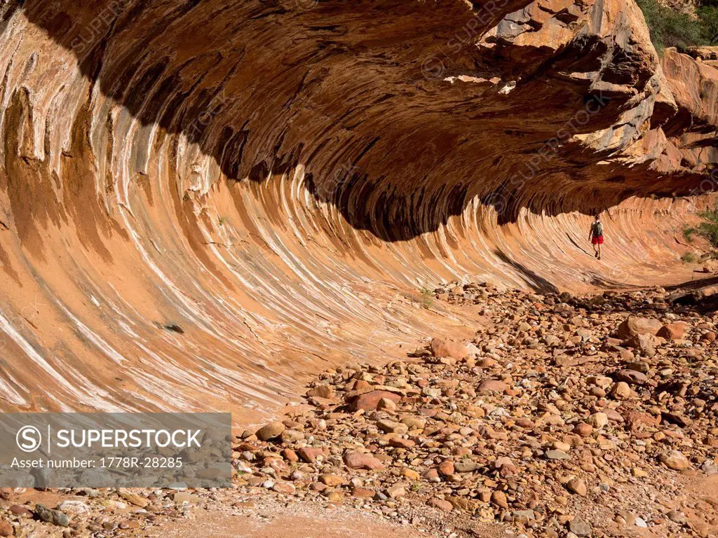 A man hiking under a rock formation that looks like a wave.