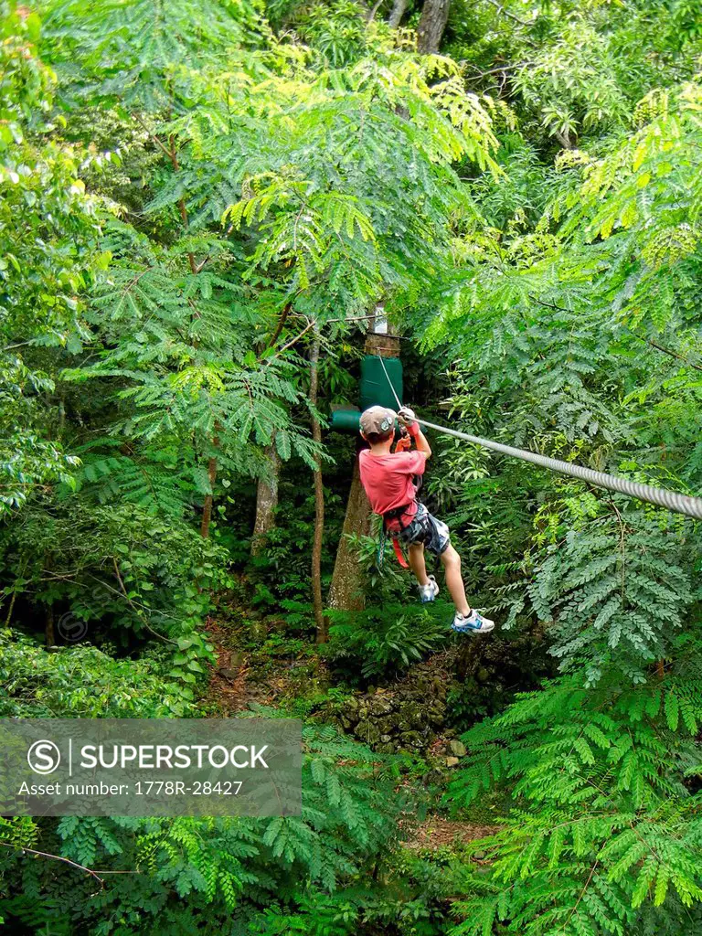 Young boy sliding down a zip line in the jungle of Saint Martin in the Caribbean.