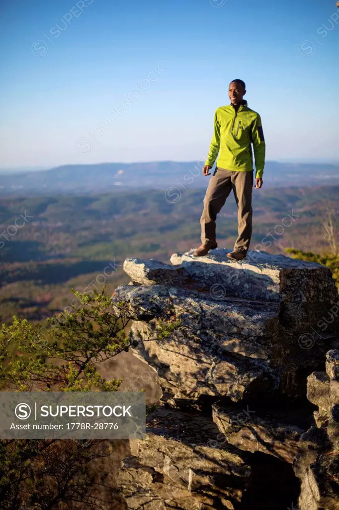 A young man stands on boulder on the edge of Mount Cheaha